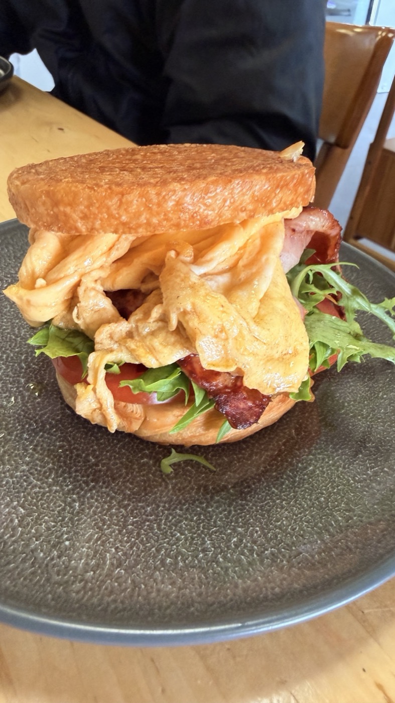 A tall breakfast burger with a fried egg, bacon, rocket and tomato on a dark plate