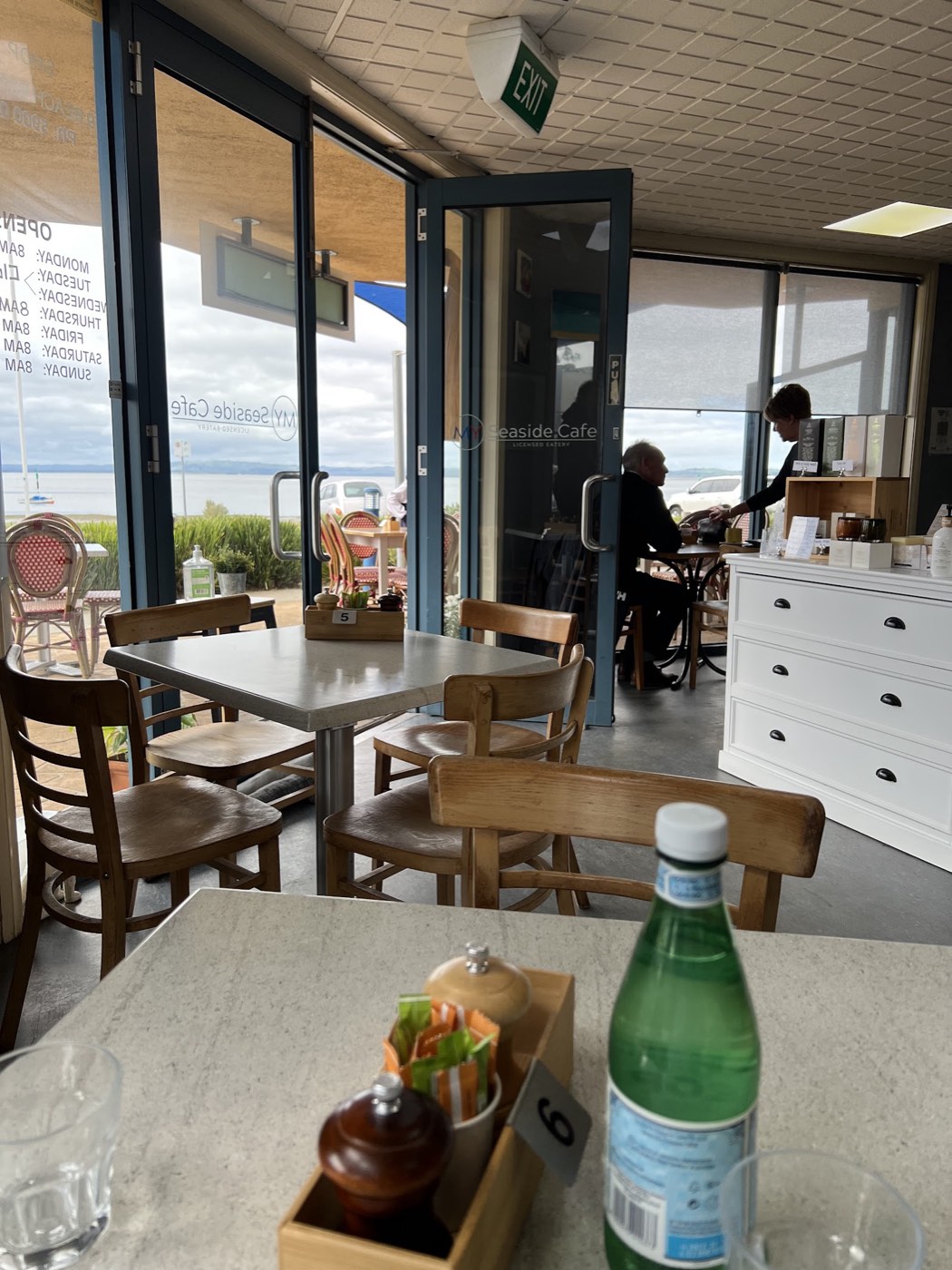 Inside the café: timber tables and chairs beside big glass doors with the water beyond