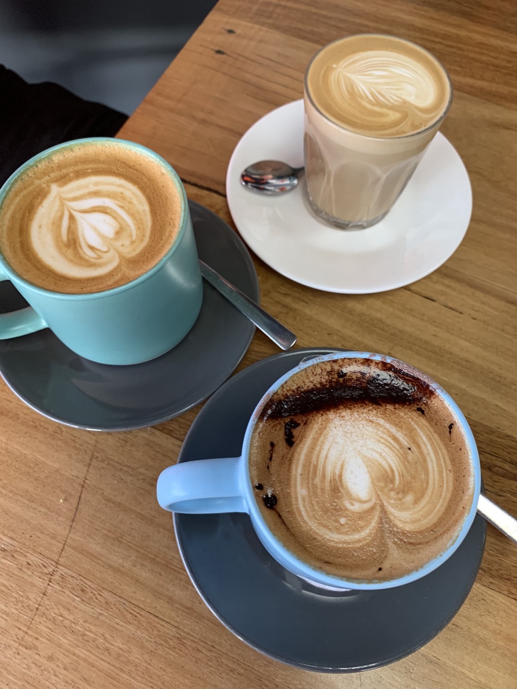 Three coffees with latte art in blue and grey cups on a timber table