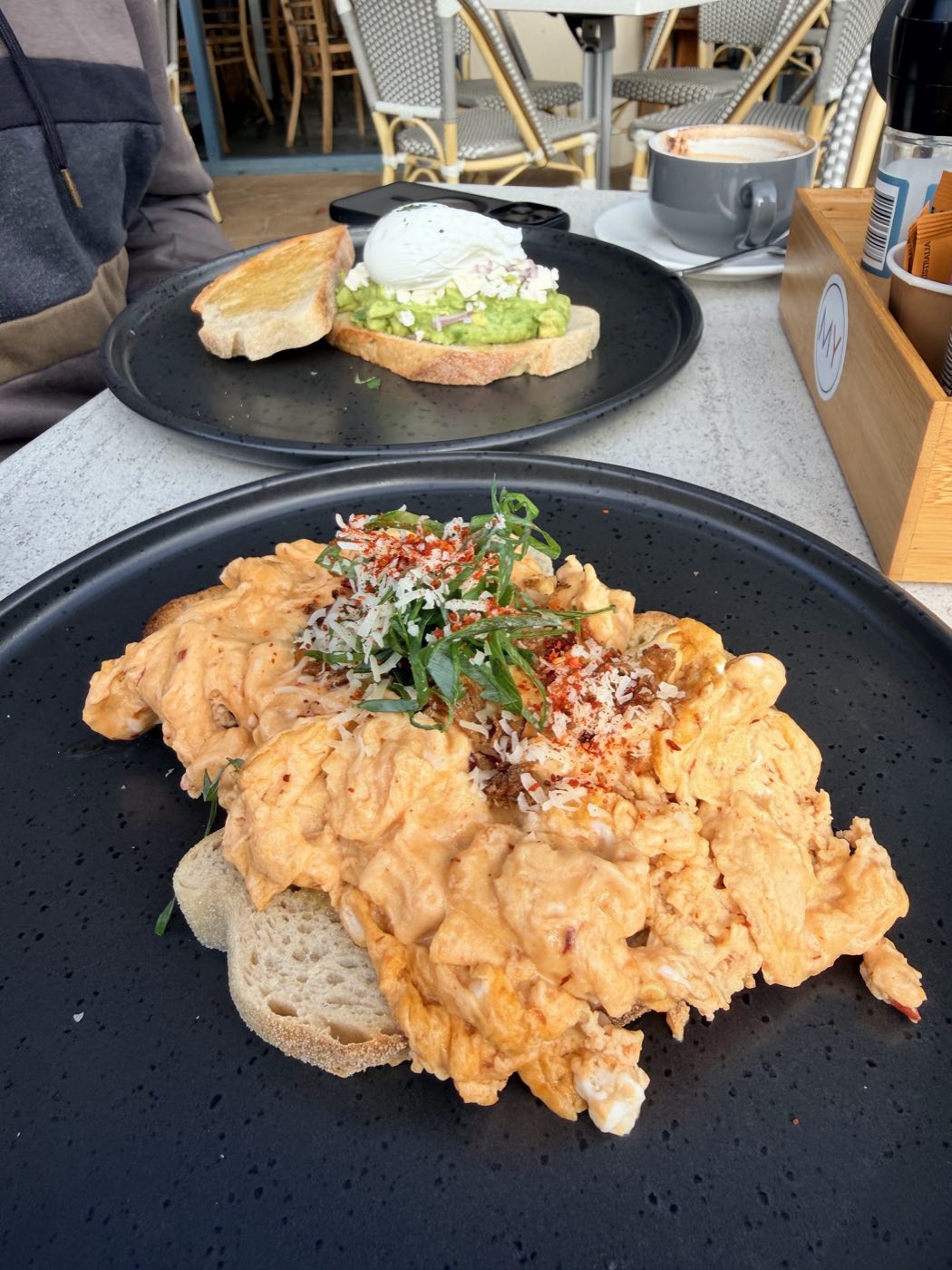 Soft scrambled eggs scattered with herbs and chilli on sourdough, with avocado toast on a plate behind