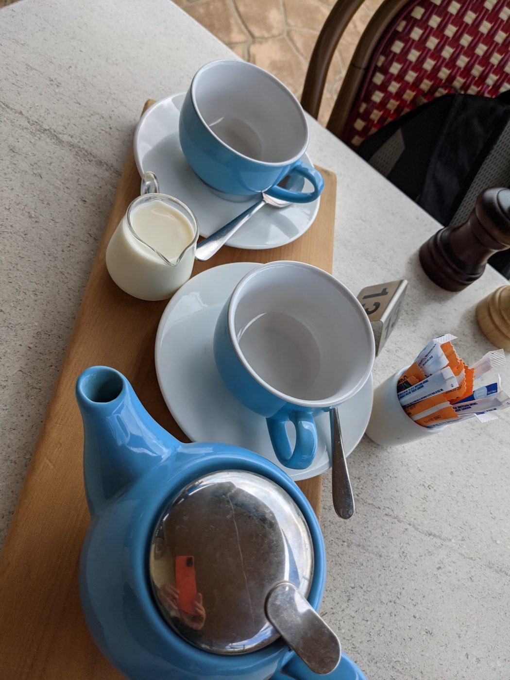 A blue teapot and two blue cups with a small jug of milk on a wooden board